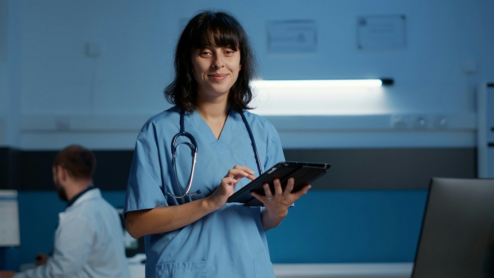 Medicinska sestra drži tablet i gleda u kameru